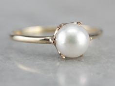 "Perfect for stacking or even to wear alone, this minimalist pearl ring is as simple as can be. Crafted of yellow gold, six prongs hold a shining pearl. Metal: 10K/14K Yellow Gold Gem: Pearl Gem Measurements: 6.7 mm, Round Ring Size: 7.75 Marks: \"10K 14K\" Stamped on the inside band SKU #: MTR5PM7R Each piece has been identified and graded by a Graduate Gemologist who has been certified by the Gemological Institute of America (GIA). We have four brick and mortar storefronts in Maine, Massachuse Minimalist Formal Round Pearl Ring, Formal Minimalist Round Pearl Ring, Minimalist Solitaire Pearl Ring For Formal Occasions, White Solitaire Pearl Promise Ring, Timeless Solitaire Pearl Ring Round Cut, Classic White Pearl Ring, Fine Jewelry Pearl Solitaire Ring With Round Band, Classic Pearl White Rings With Pearl Drop, Solitaire Pearl Ring, Fine Jewelry