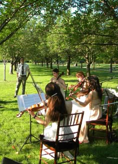 a group of people that are sitting in the grass with violin's on their laps