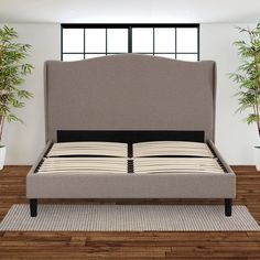 a bed sitting on top of a wooden floor next to a potted palm tree