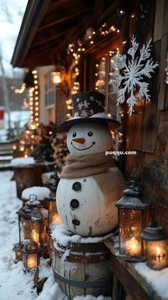 a snowman sitting on top of a barrel in front of a house covered in snow