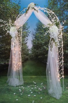 a wedding arch decorated with white flowers and fairy lights in the middle of a grassy area