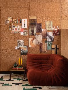 a red couch sitting in front of a cork wall with pictures on it's side