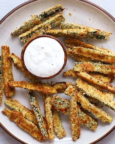 a plate topped with fried asparagus next to a small bowl of ranch dressing