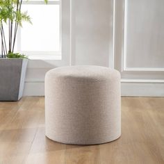 a round ottoman sitting on top of a wooden floor next to a potted plant