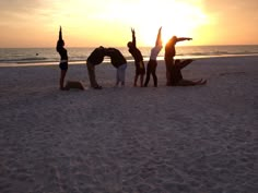 four people doing yoga on the beach at sunset with their hands up in the air