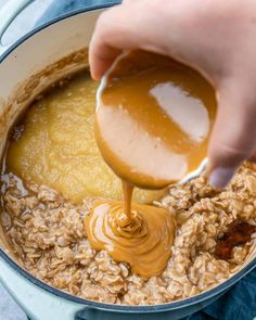 someone pouring peanut butter on top of oatmeal in a pot with other ingredients