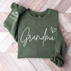 a green sweatshirt with the word grandma written in white on it, sitting on a wood floor