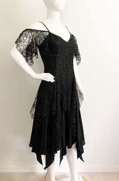 "Get ready to party in this fabulous off the shoulder dress from Nuance, made in USA.  The body of the dress is black with a floral lace overlay that has free form gold dots throughout.  The flirty hemline is handkerchief, high low style.  Each triangle section is separate, so the dress is full of movement and peaks of leg.  The bodice has spaghetti straps and off the shoulder lace \"sleeves\".  Great 80's look.  Size tag 9, check measurements carefully, no stretch.  Fits mannequin 35X26X33. Mea Vintage Dresses Black, 80s Party Dress, Black 80s, Party Dress Lace, 80's Party, 80s Look, Handkerchief Hem Dress, Handkerchief Dress, 1980s Fashion