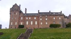 an old castle with stairs leading up to the front door and green grass in front