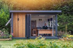 a man sitting at a desk in the back of a small shed with open doors