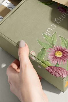 a person's hand is holding the edge of a box with flowers painted on it