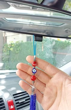 a hand holding a blue and red beaded keychain hanging from the side of a car