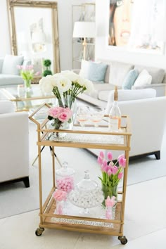 an instagram photo with pink flowers on a gold serving cart and white couches in the background