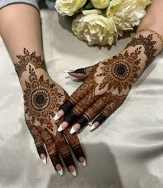 two hands with henna designs on them and flowers in the background, one being held up