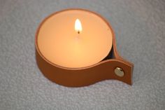 a lit candle sitting on top of a white table next to a brown leather holder