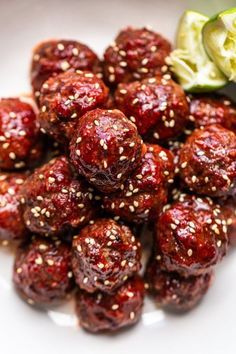 a white plate topped with meatballs covered in sesame seeds next to a cucumber