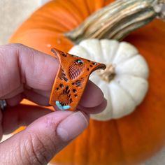 a hand holding an orange piece of wood in front of a pumpkin and other decorations