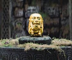 a golden buddha statue sitting on top of a black pot filled with grass and dirt