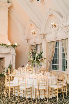 the tables are set with white linens and gold chairs, along with flowers in tall vases