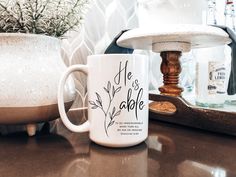 a white coffee mug sitting on top of a counter next to a potted plant