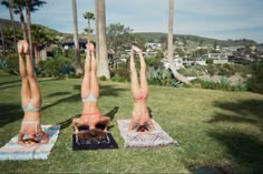 two women in bikinis doing handstand yoga on towels with palm trees in the background