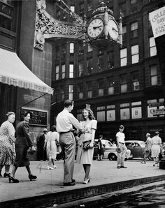 an old black and white photo of people standing on the sidewalk in front of buildings