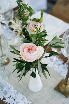 two vases filled with pink flowers on top of a white lace tablecloth covered table