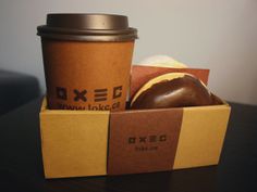 a coffee cup sitting next to a donut in a box on top of a table