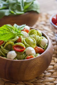 a wooden bowl filled with pesto pasta and basil sprinkled on top of it