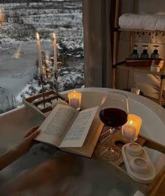 a person sitting in a bathtub reading a book with candles on the side and an open book next to them