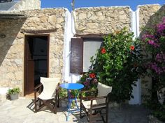 two chairs and a table in front of a stone building with flowers growing on it