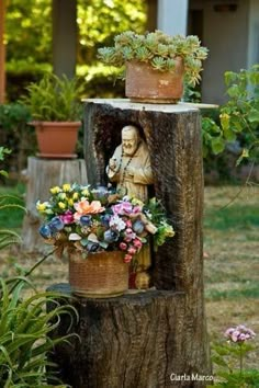 a tree stump with flowers and a statue in it's center surrounded by potted plants