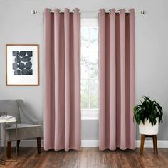 a living room with pink curtains and a chair in front of a window that has a potted plant next to it