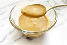 a spoon full of peanut butter sits in a glass bowl on a marble countertop