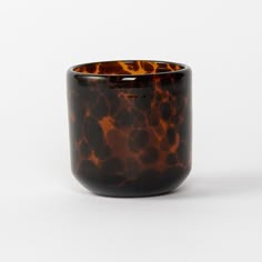 a brown and black glass vase sitting on top of a white table next to a wall