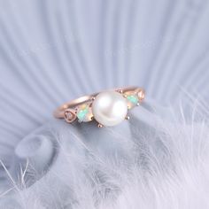 an opal and diamond ring sits on top of a white feathers feather with the light shining through it