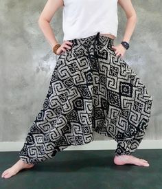 a woman standing in front of a concrete wall with her hands on her hips, wearing black and white patterned pants