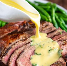 a person pouring sauce on top of some meat with green beans and asparagus