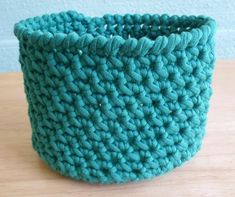 a blue crocheted basket sitting on top of a wooden table next to a wall