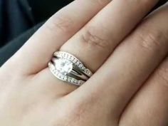 a woman's hand holding an engagement ring with a diamond in the middle and two bands on it