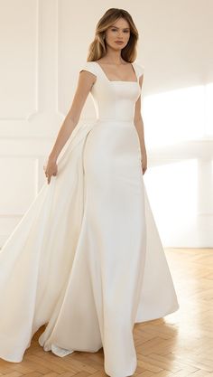 a woman in a white wedding dress standing on a wooden floor with her arms behind her back