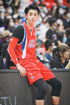 a young man sitting on top of a bench in front of a crowd at a basketball game