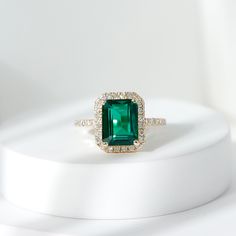 an emerald and diamond ring sitting on top of a white surface with diamonds around it