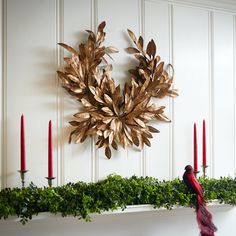 a wreath is hanging on the wall above a mantel with candles and greenery