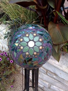 a colorful glass ball sitting on top of a metal stand next to flowers and plants