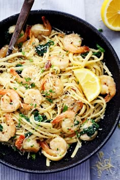 a skillet filled with pasta and shrimp on top of a blue table cloth next to lemon wedges