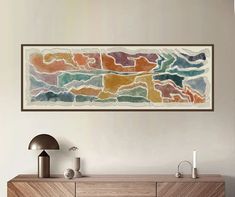 an abstract painting hangs on the wall above a wooden cabinet in a modern living room