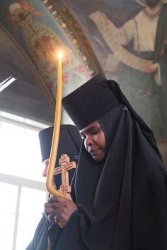 a nun holding a candle in her hand and wearing a black robe with a cross on it