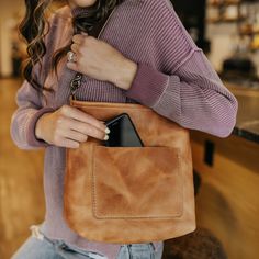 a woman is holding a brown purse in her right hand and smiling at the camera