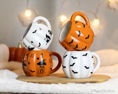 two coffee mugs with bats painted on them sitting on a wooden board in front of a christmas tree